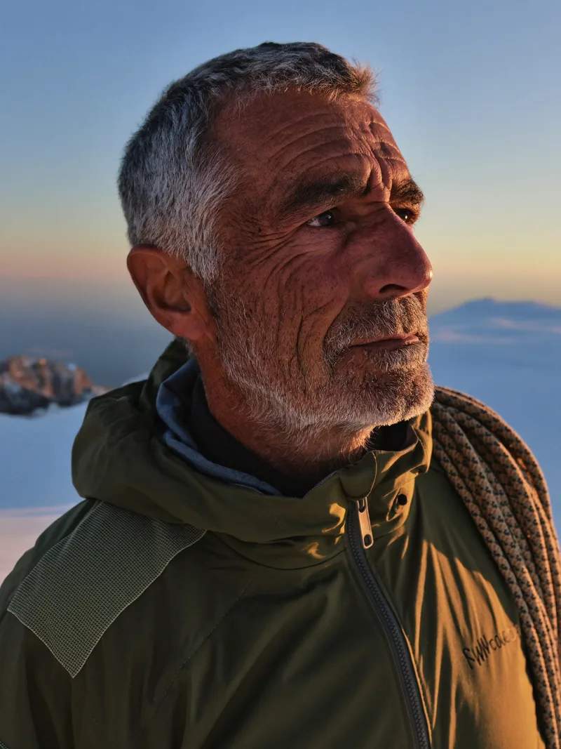 Elias Rott, mountain guide, rope coiled over his shoulder, watching the horizon at dusk