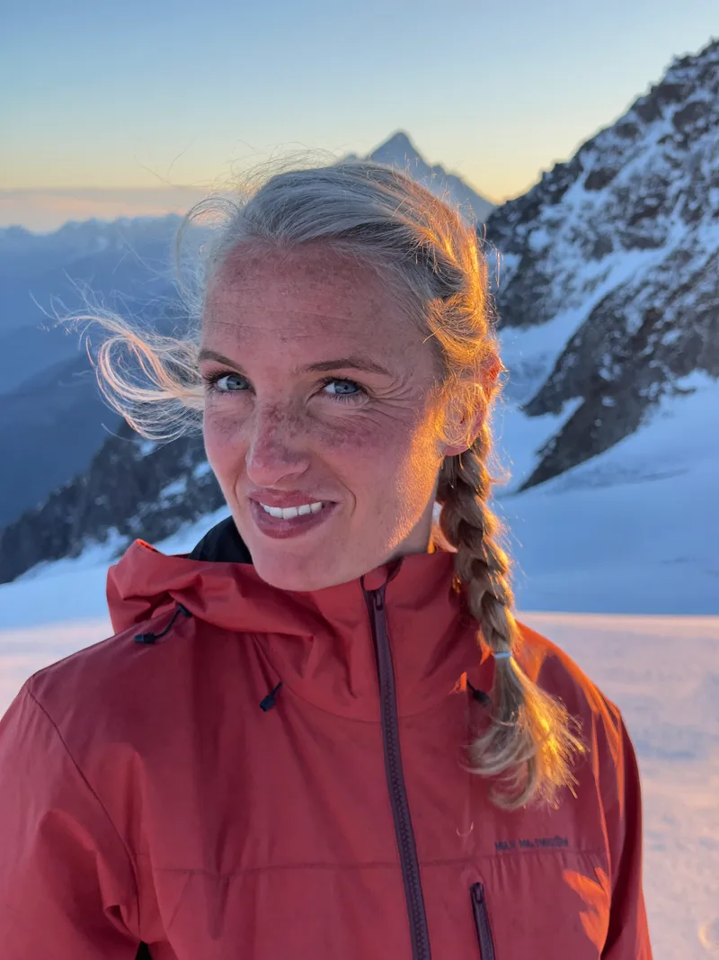 Mara Vollen, mountain guide, at golden hour on a glacier ridge, wind in her braided hair